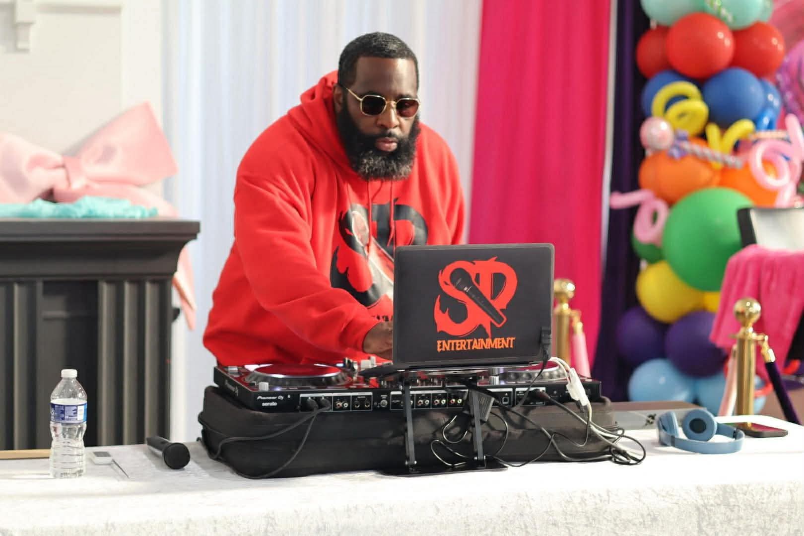 DJ Stevie Steve working the controller at a celebration decorated with colourful balloons and pink drapes