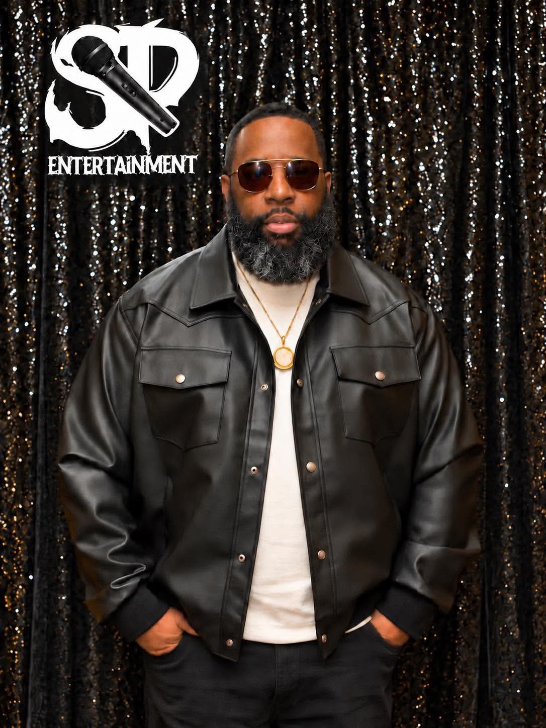 Studio portrait of Stevie Pugh in a black leather jacket and tinted sunglasses against a black sequin backdrop